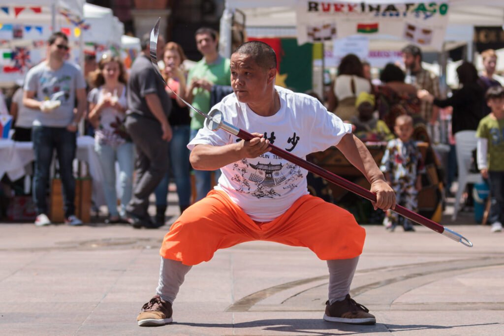 Expert de kung-fu en pleine action sur la Place du Capitole à Toulouse, démontrant une technique avancée devant un public captivé