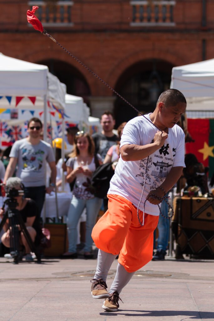 Maître de kung-fu réalisant une démonstration technique sur la Place du Capitole à Toulouse, avec des spectateurs en arrière-plan.